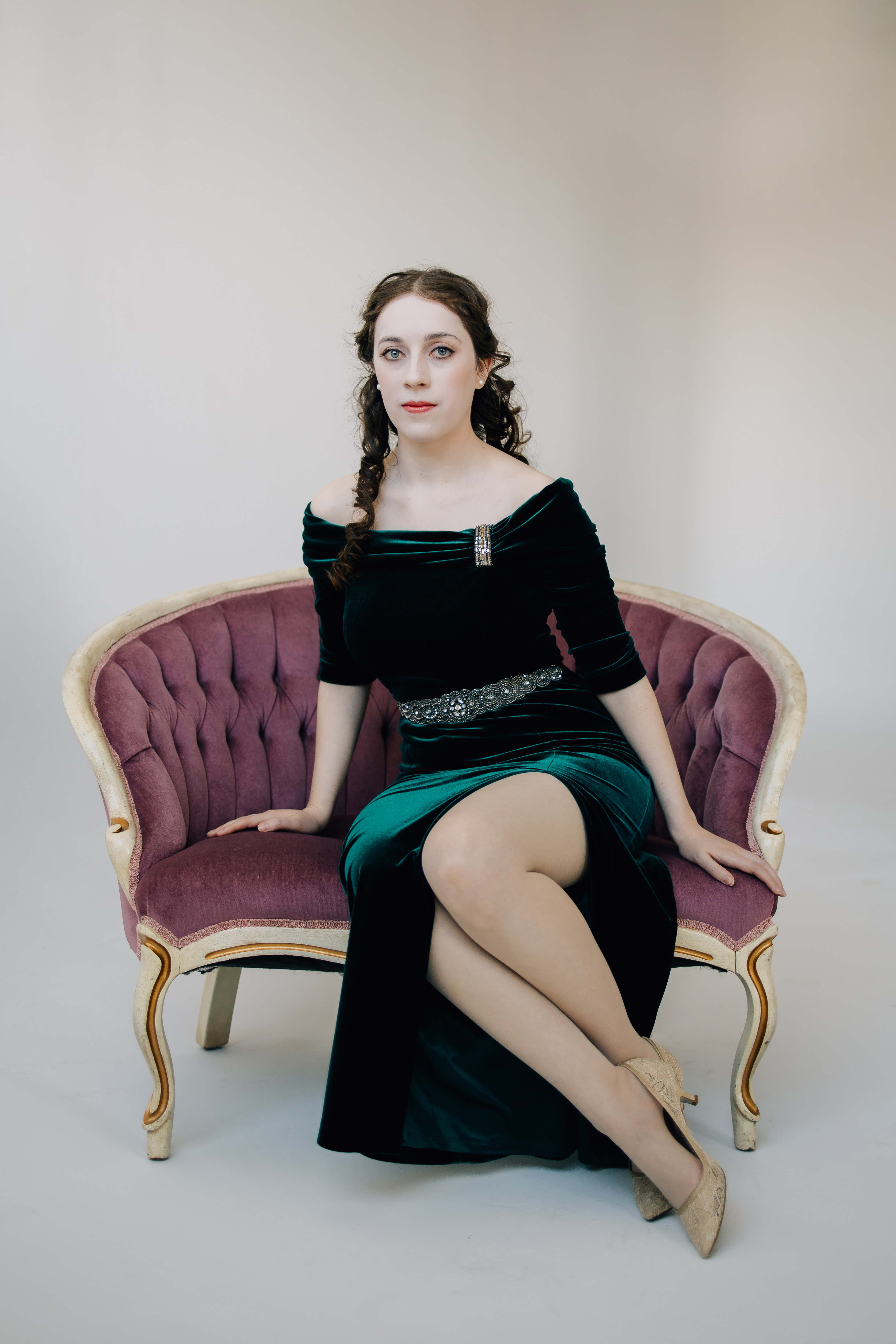 Young woman in green velvet gown sitting on pink velvet chair.